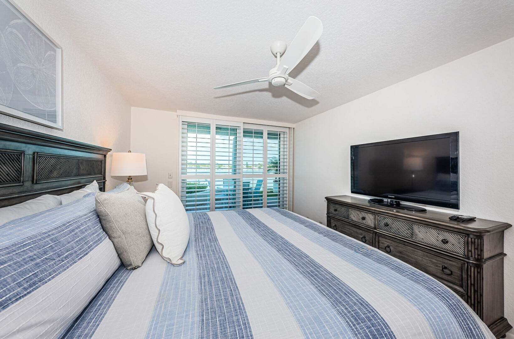 Una habitación de hotel con una cama, un televisor, un ventilador de techo y una ventana con persianas.