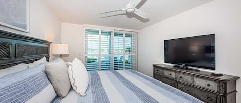 Una habitación de hotel con una cama, un televisor, un ventilador de techo y una ventana con persianas.