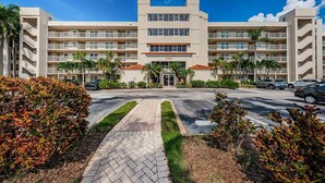 A multi-story hotel with a central entrance, surrounded by palm trees and a paved driveway.