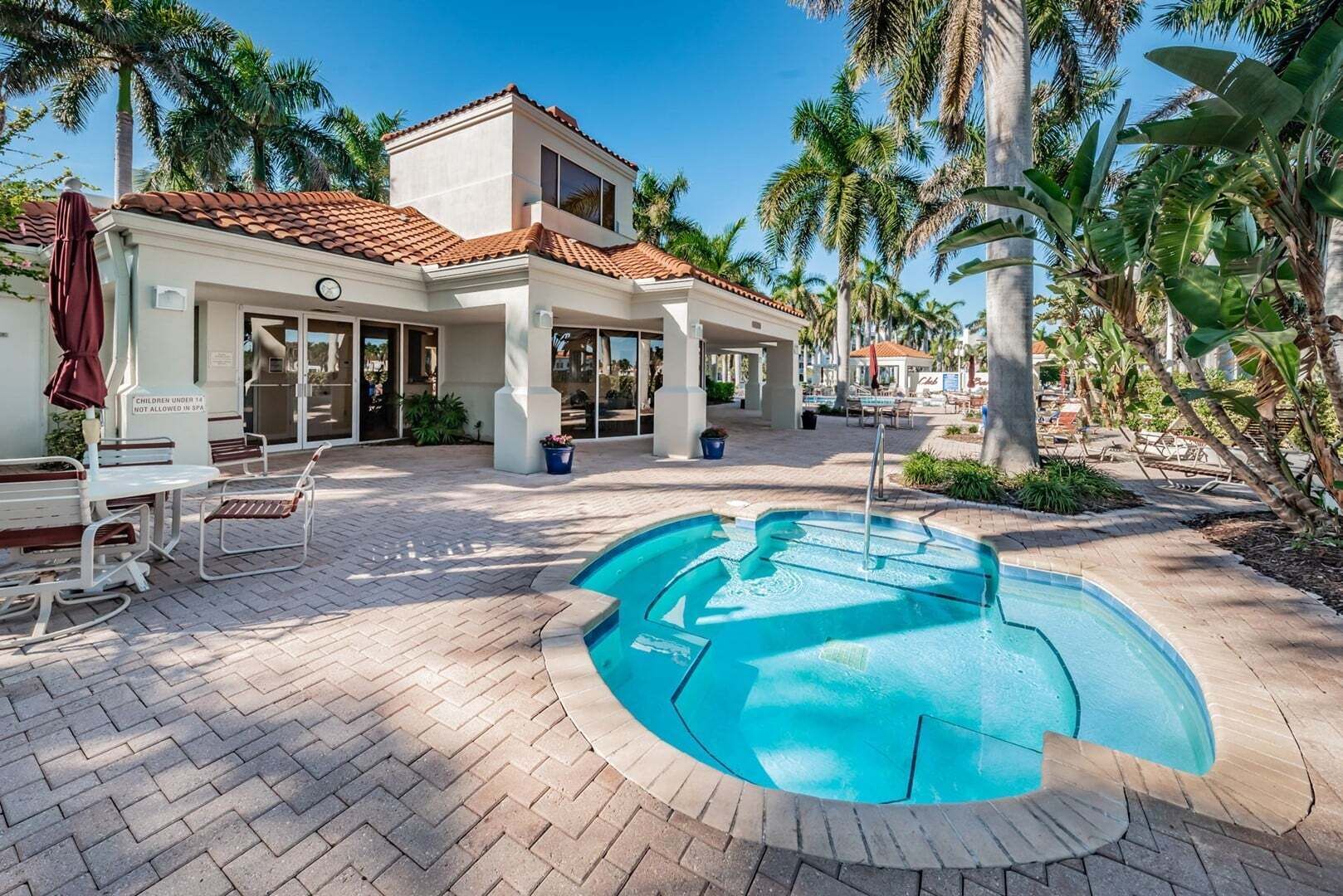 A pool area with a tiled deck, lounge chairs, and a building with a tiled roof and large windows.