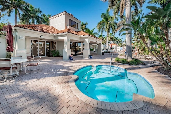 A pool area with a tiled deck, lounge chairs, and a building with a tiled roof and large windows.