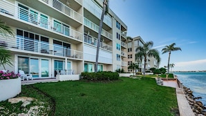 A multi-story hotel with balconies, a grassy lawn, and a view of the water.