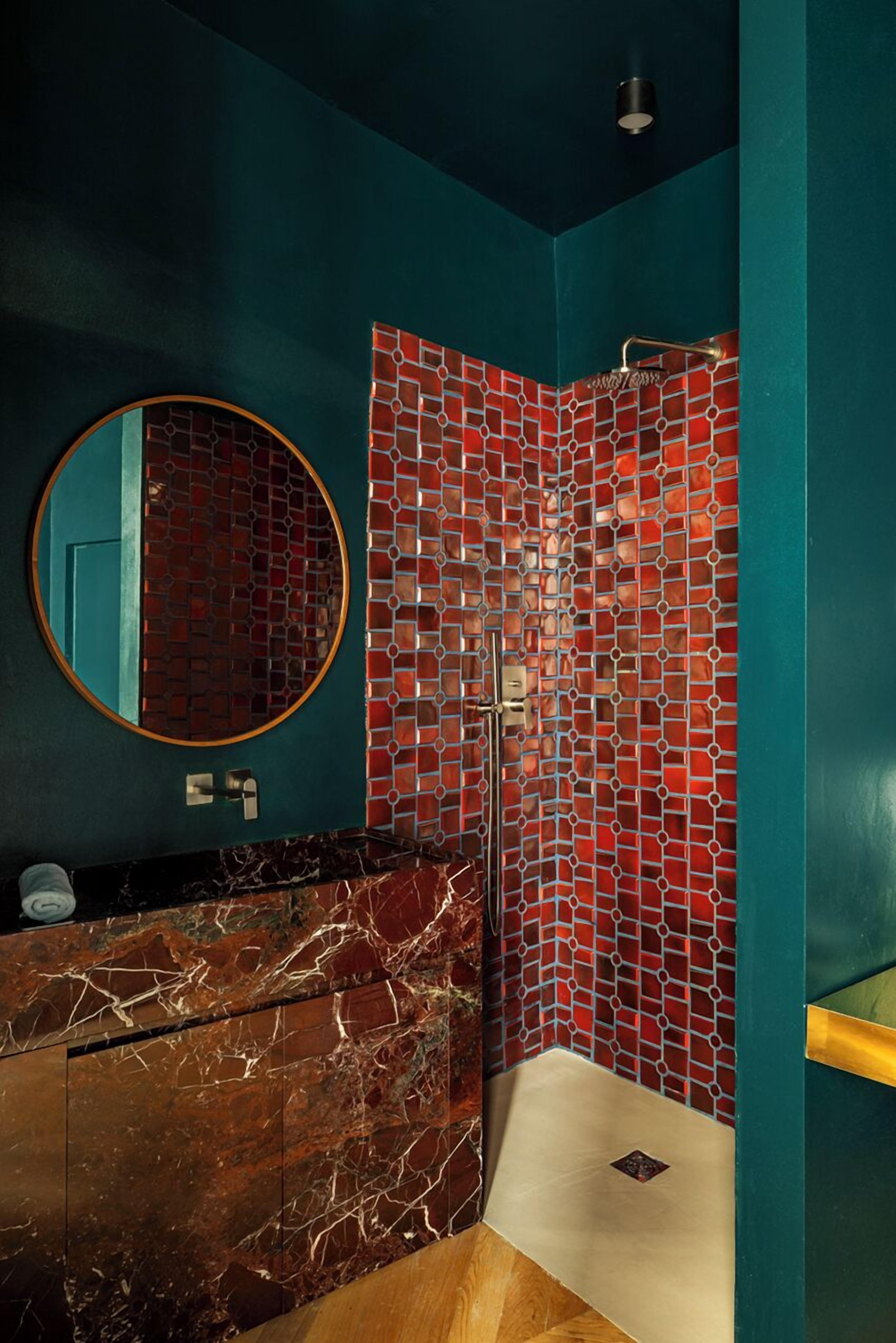 Un baño con pared verde azulado, un lavamanos de mármol, ducha con mosaico rojo y un espejo redondo.