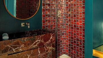 Un baño con pared verde azulado, un lavamanos de mármol, ducha con mosaico rojo y un espejo redondo.