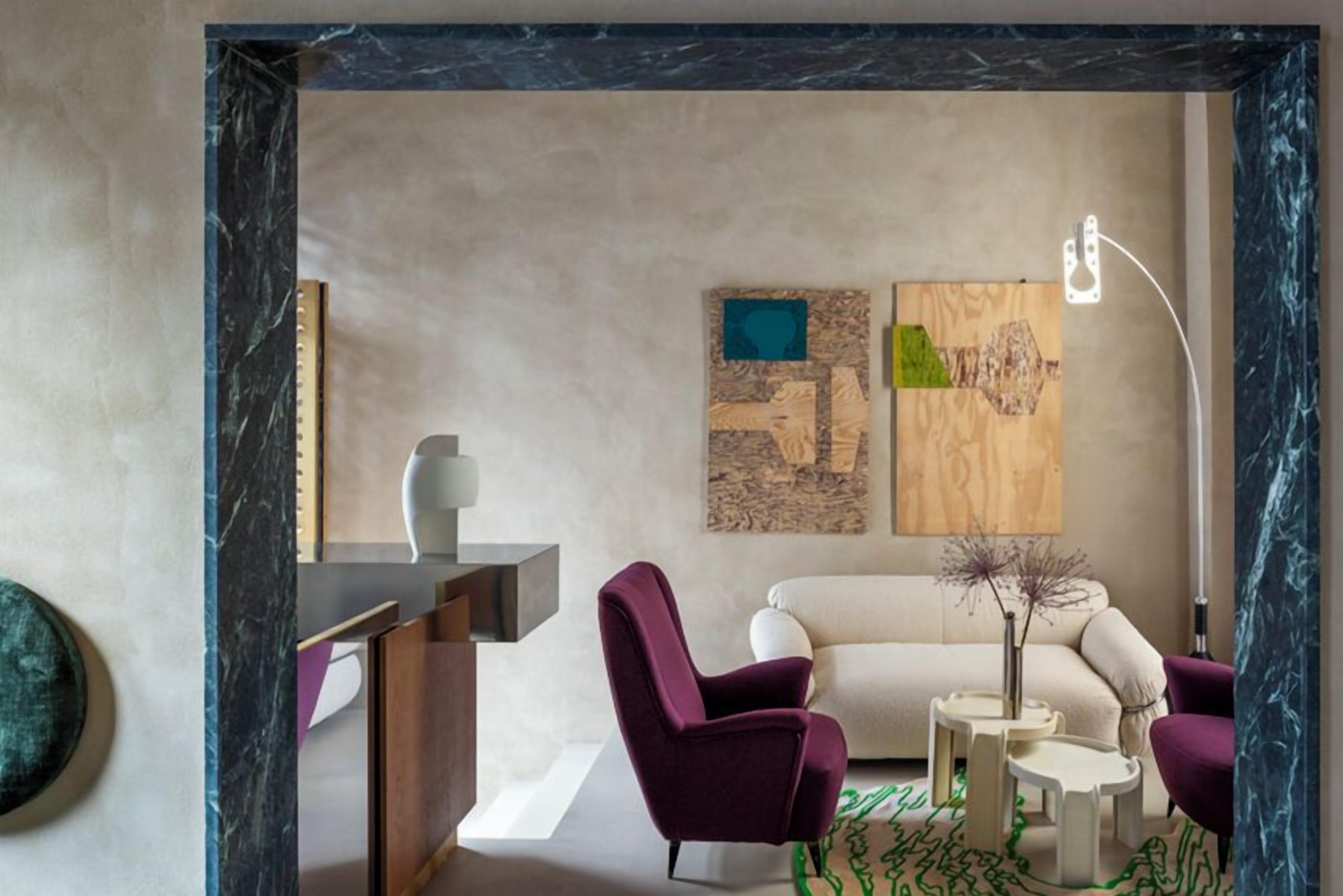 A modern living room with a marble-framed doorway, a sofa, two armchairs, a coffee table, and abstract wall art.