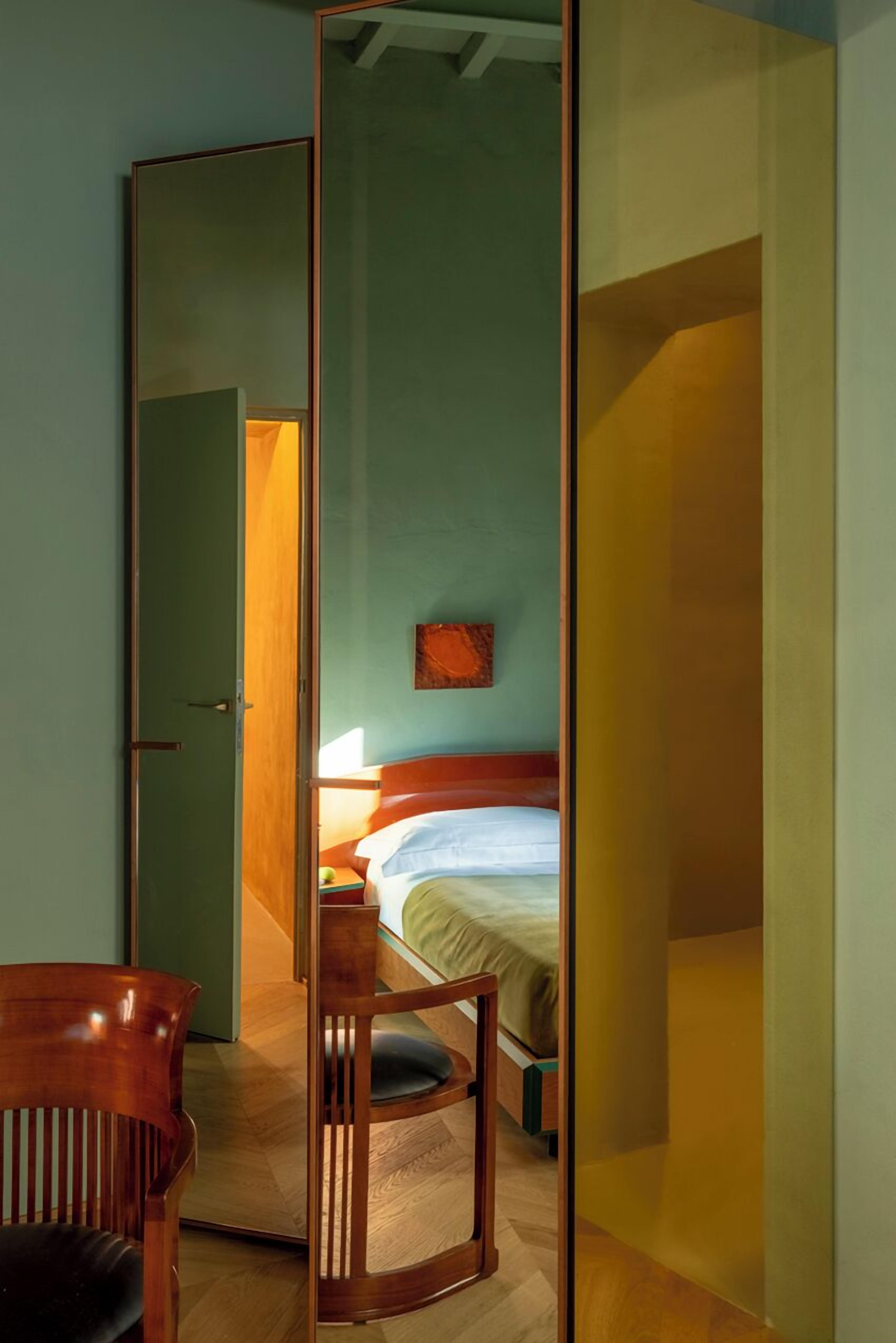 Une chambre d’hôtel avec un lit, une table de chevet, une chaise et un miroir.