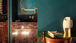 Un baño moderno con tocador de mármol, un espejo redondo y una silla de madera.