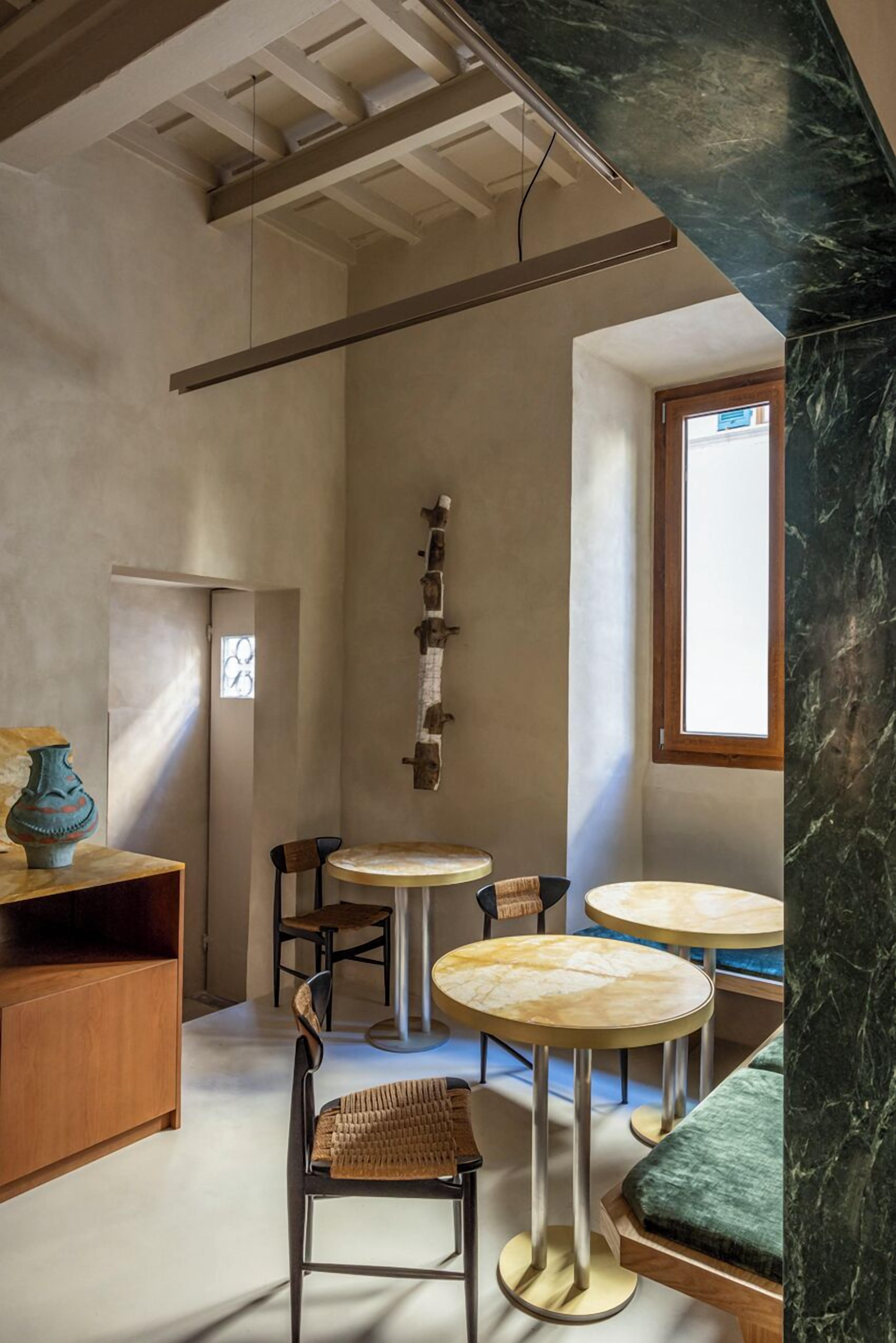 A modern interior with a high ceiling, a wooden cabinet, a vase, and a seating area with round tables and chairs.