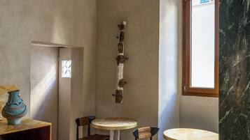 A modern interior with a high ceiling, a wooden cabinet, a vase, and a seating area with round tables and chairs.