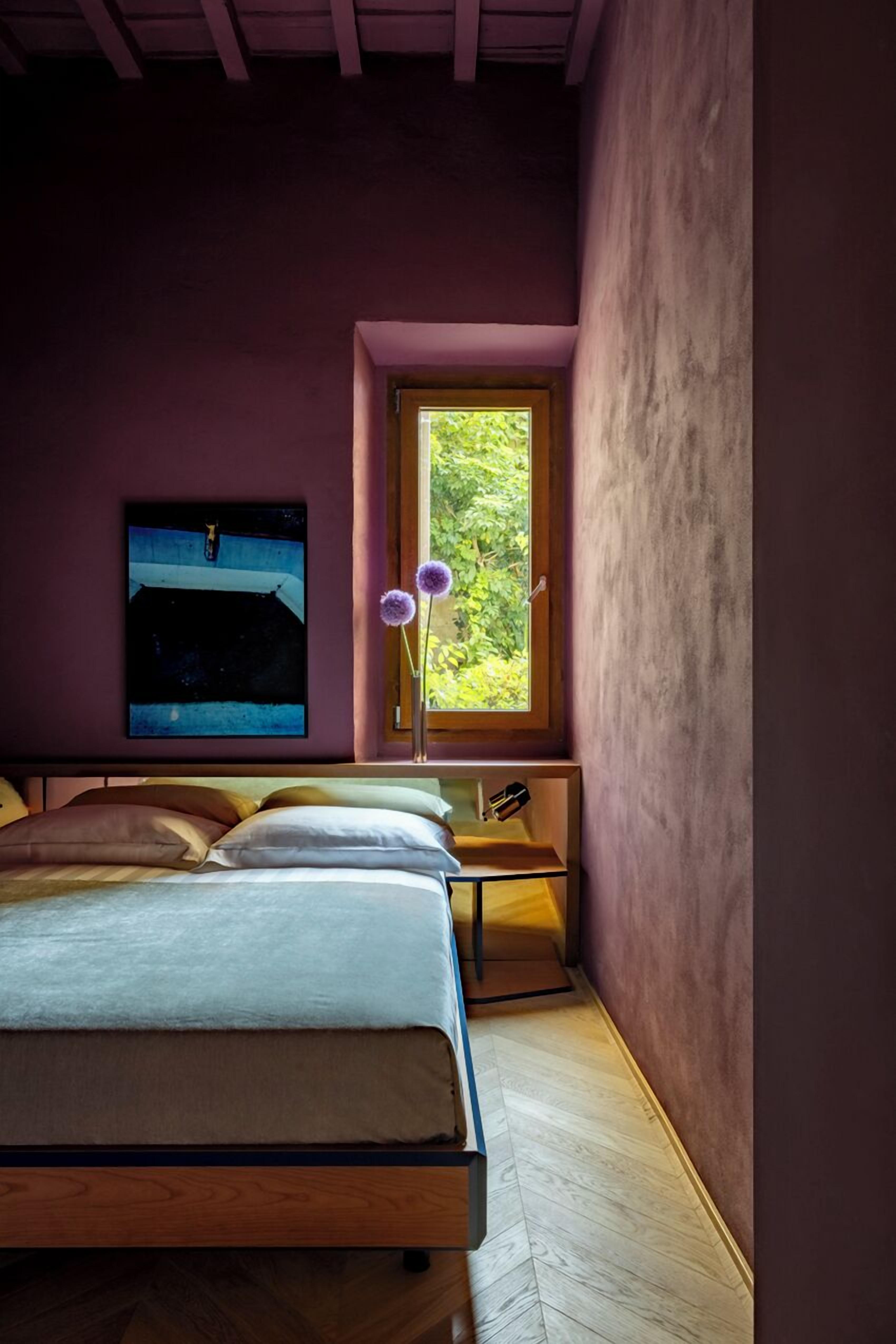 A bedroom with a bed, a window with a view of greenery, and a painting on the wall.