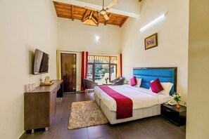 A hotel room with a large bed, a desk with a flat-screen TV, a ceiling fan, and a view of the outdoors.