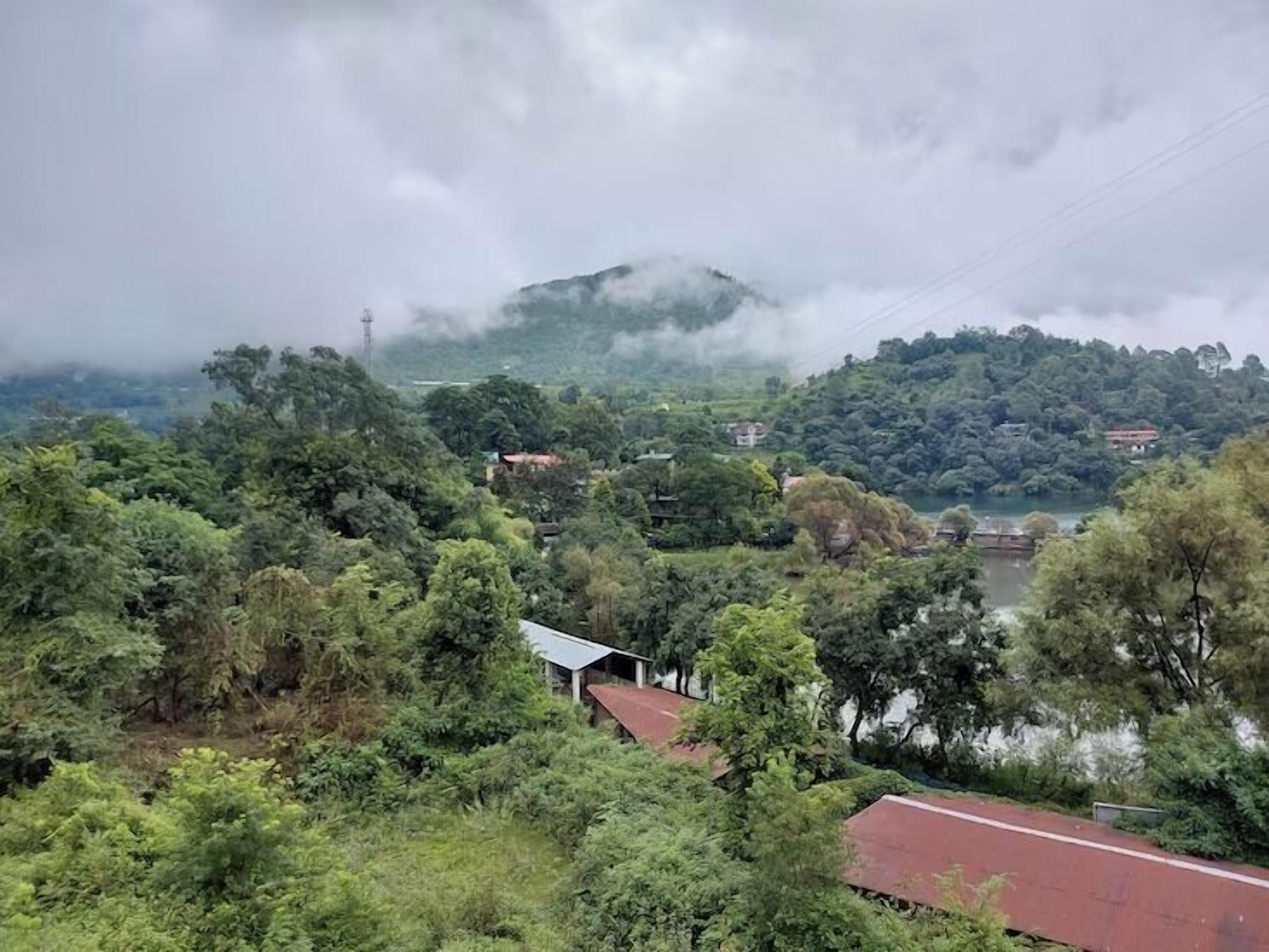 Un paysage verdoyant et luxuriant, avec une rivière, une colline sur laquelle se trouve une maison et un bâtiment au toit rouge.