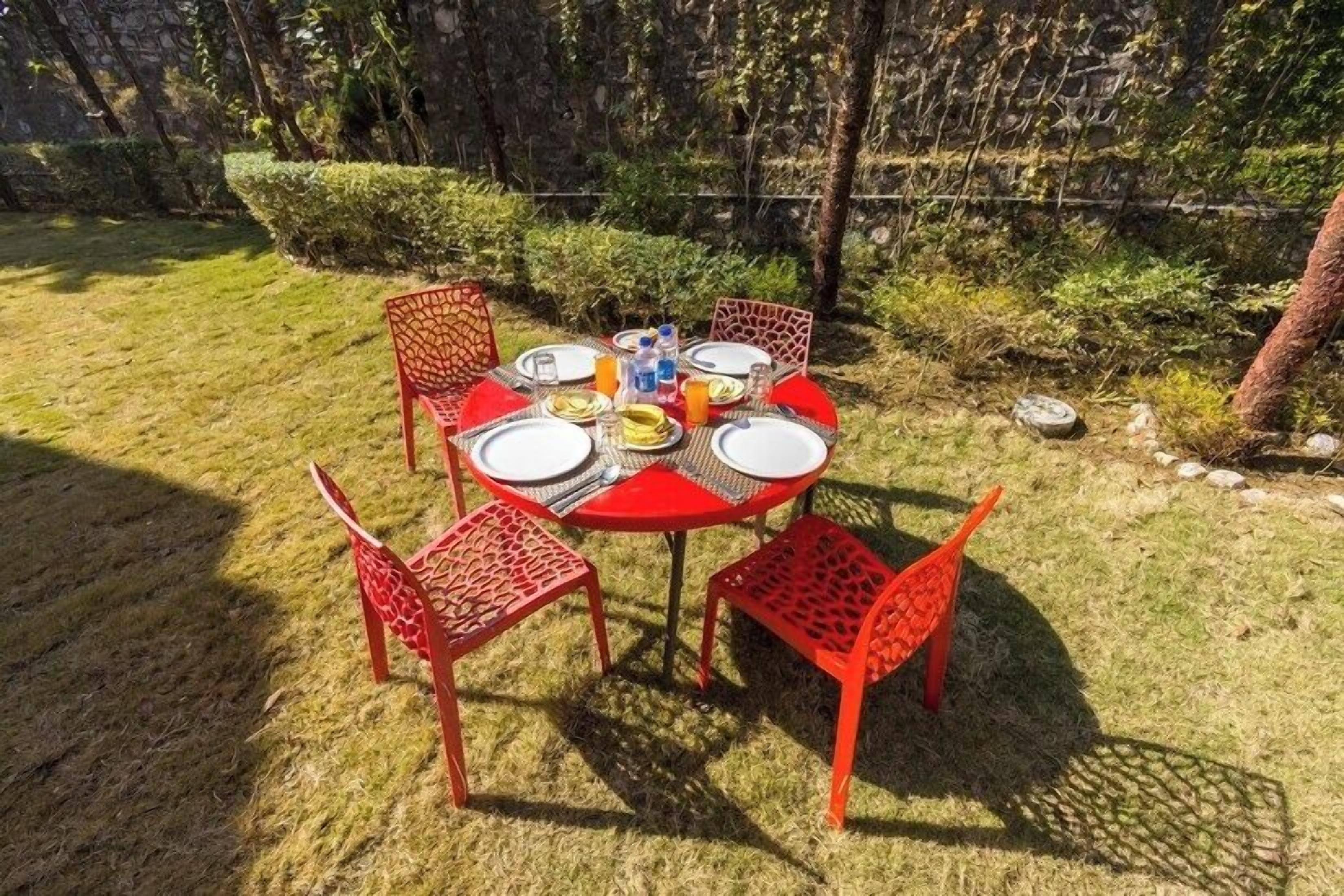 An outdoor dining area with a round table set for four, surrounded by red chairs with intricate patterns.