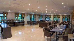 Un vaste espace de restauration dans l’hôtel, avec de nombreuses tables et chaises, un long comptoir et de grandes fenêtres dotées de rideaux.