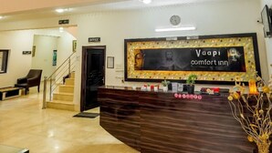 Un hall d’hôtel avec un comptoir d’accueil, un escalier et un lustre.