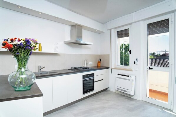 Una cocina moderna con armarios blancos, estufa a gas, horno y campana extractora integrada, además de una ventana con persianas.