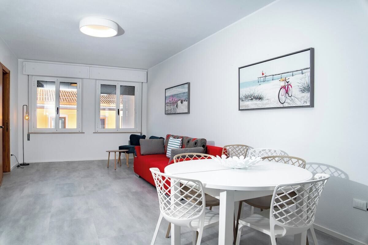 A modern living room with a red sofa, white chairs, a round table, and artwork on the walls.