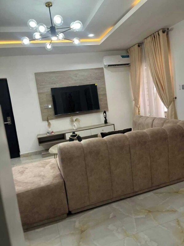 Una sala de estar moderna con un sofá modular, un televisor de pantalla plana en la pared y una lámpara de techo.