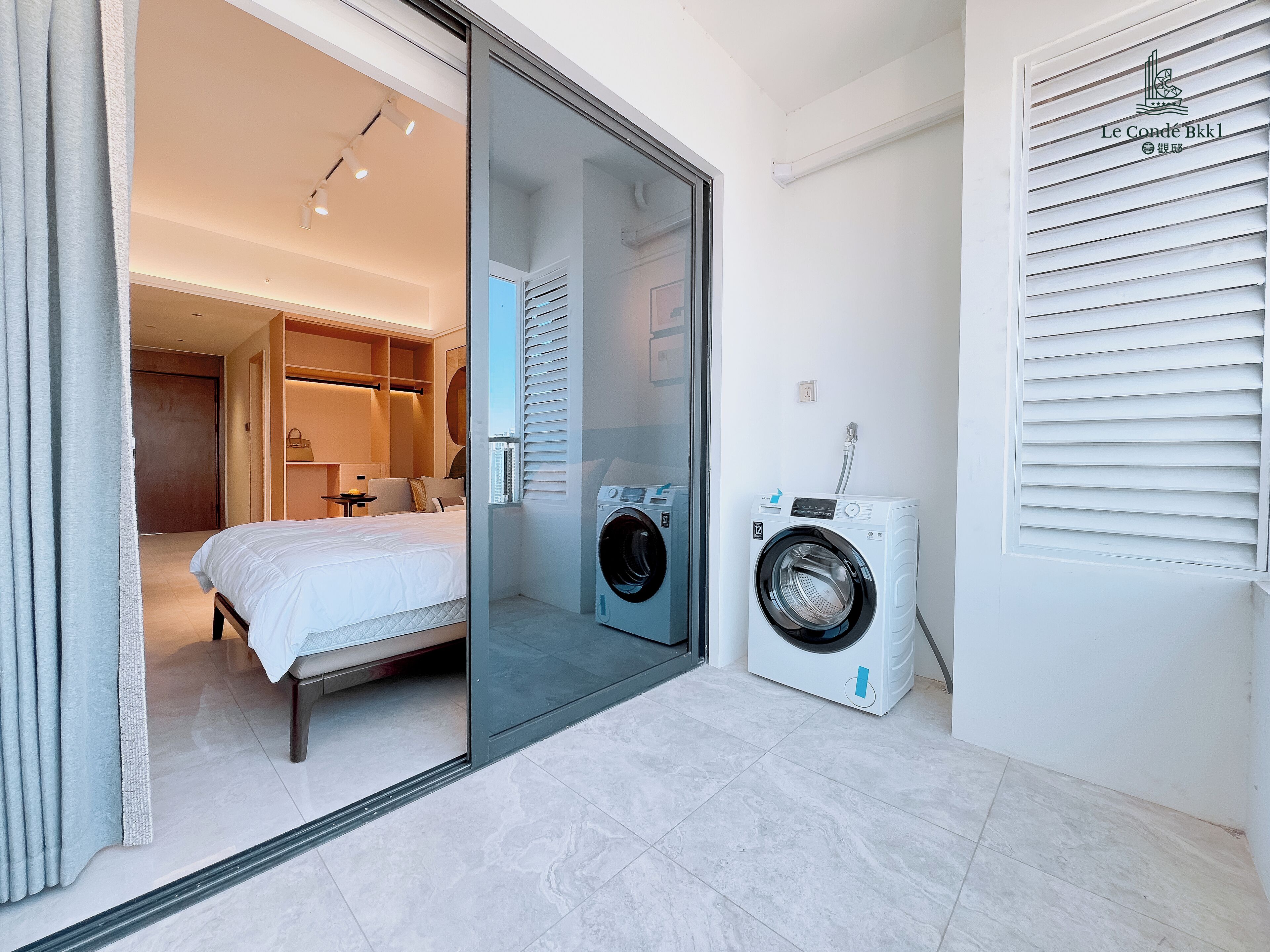 A hotel room with a bed, a washing machine, and a sliding glass door leading to a bathroom.