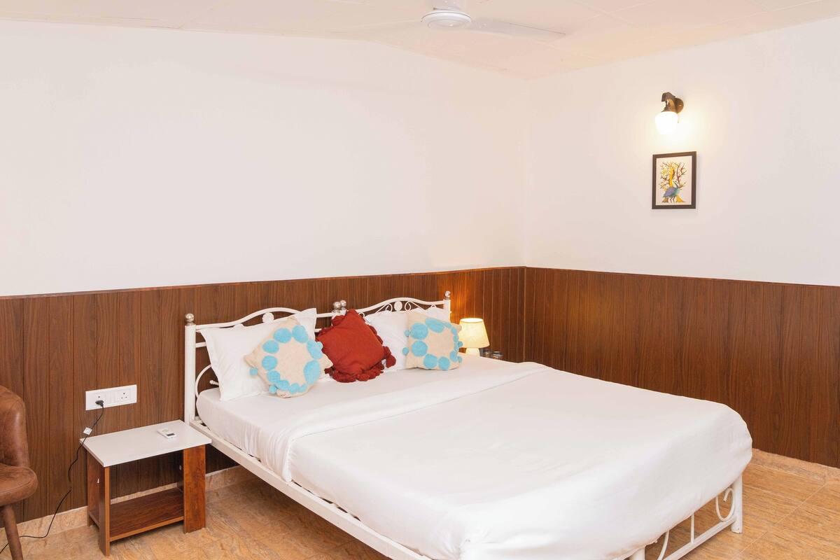 Un lit bien fait, avec une literie blanche et des coussins décoratifs, une table de chevet avec une lampe et un luminaire fixé au mur.