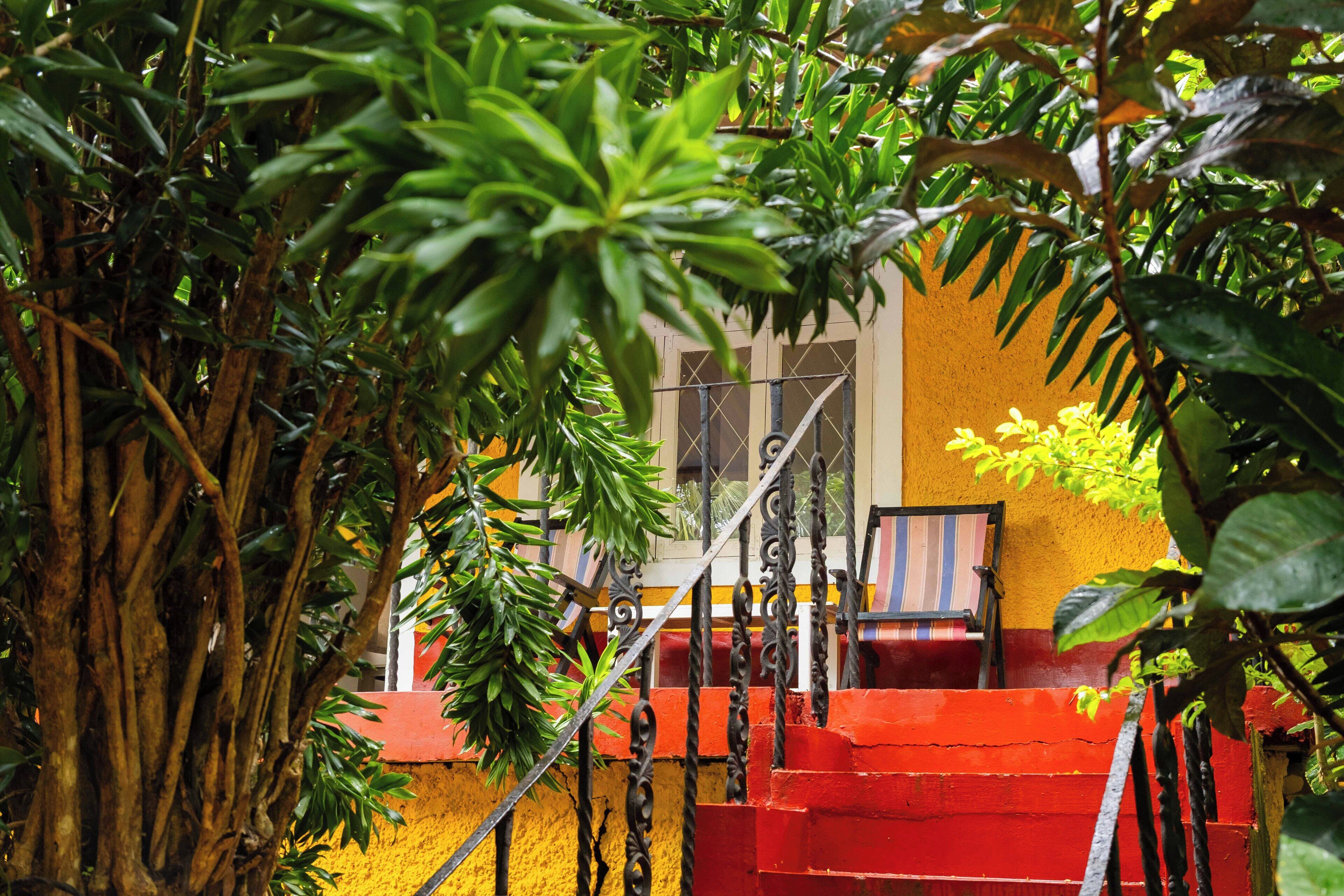 Una escalera roja que lleva a un edificio amarillo con una ventana y una silla a rayas en el exterior.