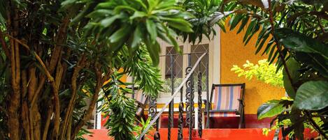 Una escalera roja que lleva a un edificio amarillo con una ventana y una silla a rayas en el exterior.