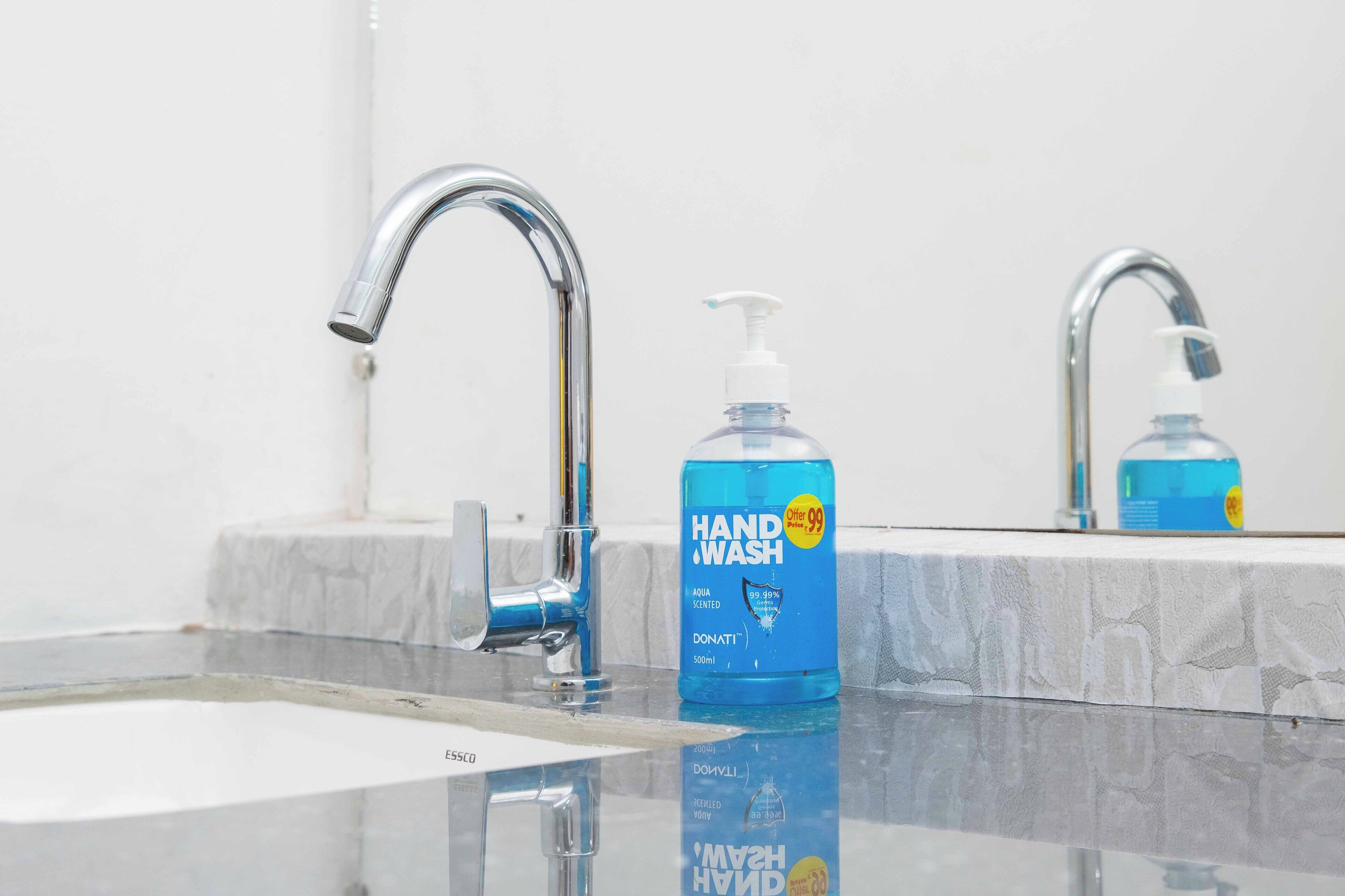 A bathroom with a modern faucet, a hand wash dispenser, and a mirror reflecting the sink area.