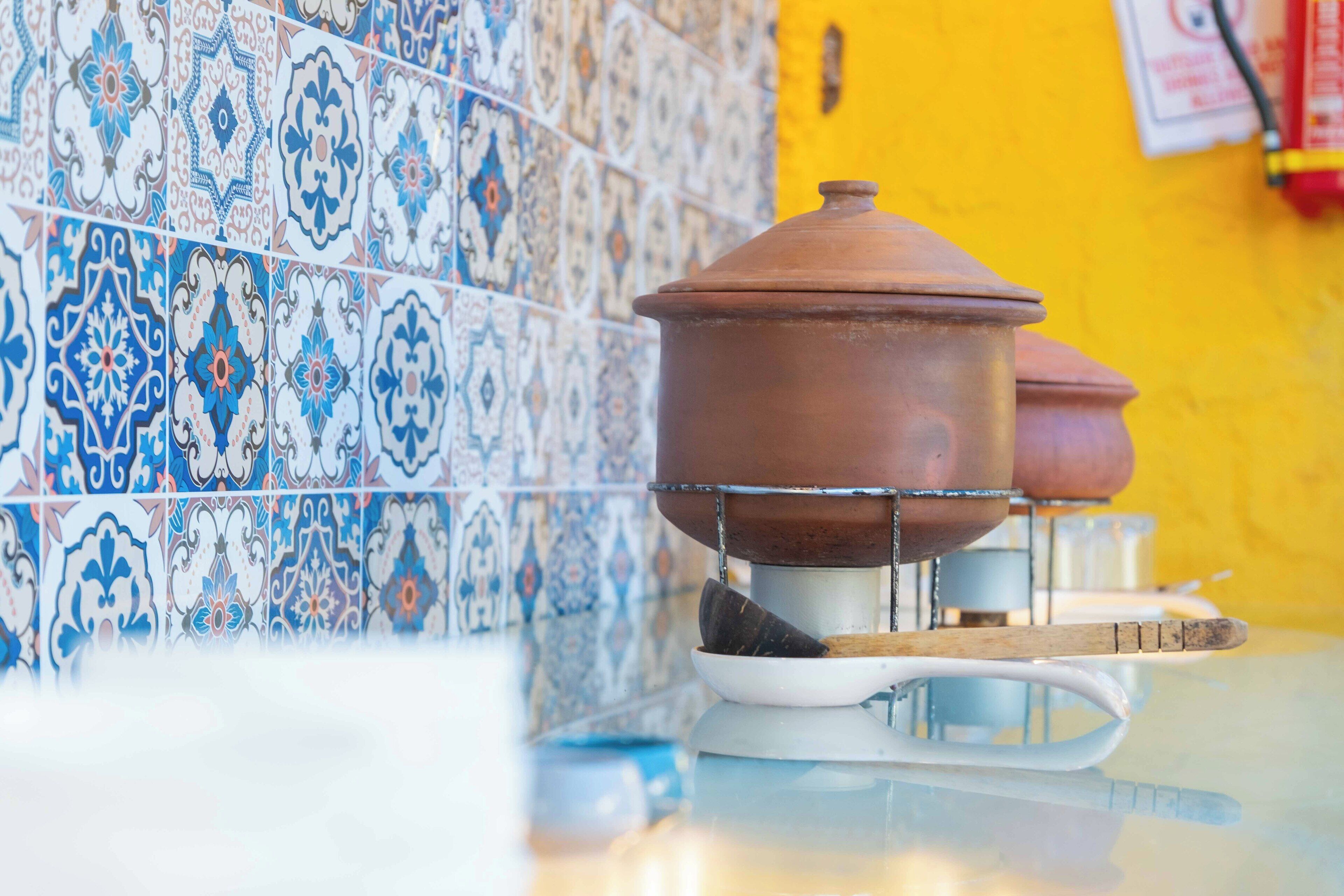 A kitchen with a tiled backsplash and a pot on a stand.