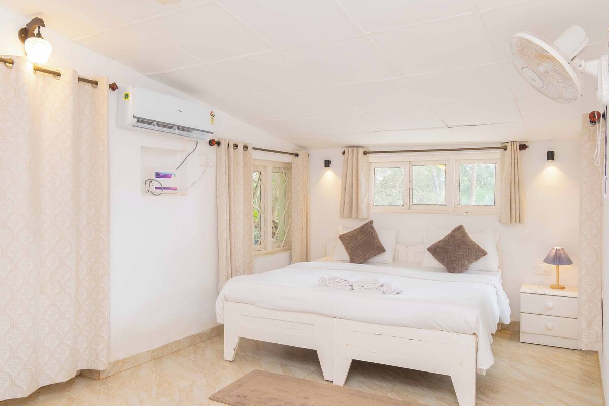 Une chambre à coucher comprenant un lit, des tables de chevet, un ventilateur et un appareil de climatisation.