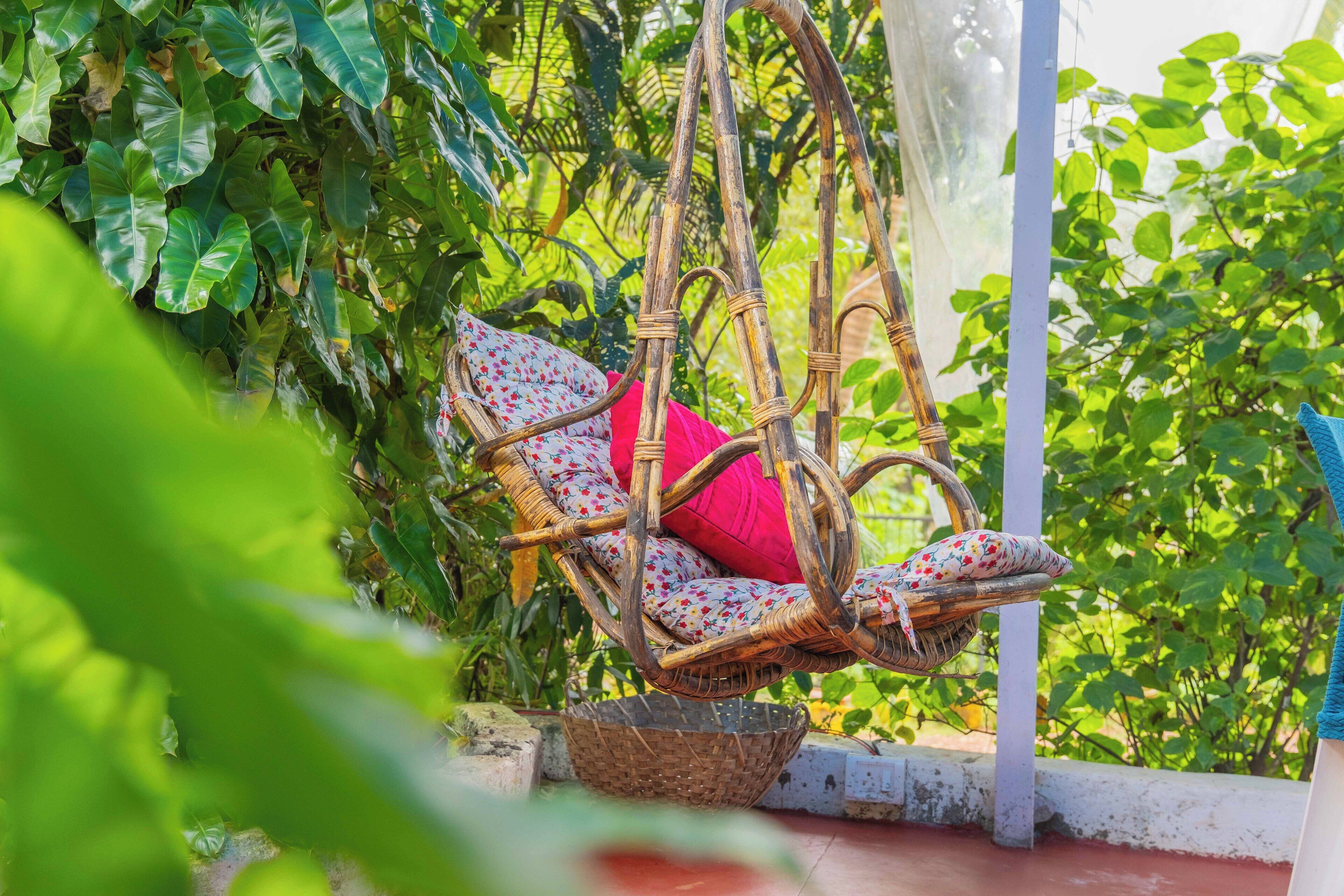 A wicker swing chair with floral cushions in a lush garden setting.