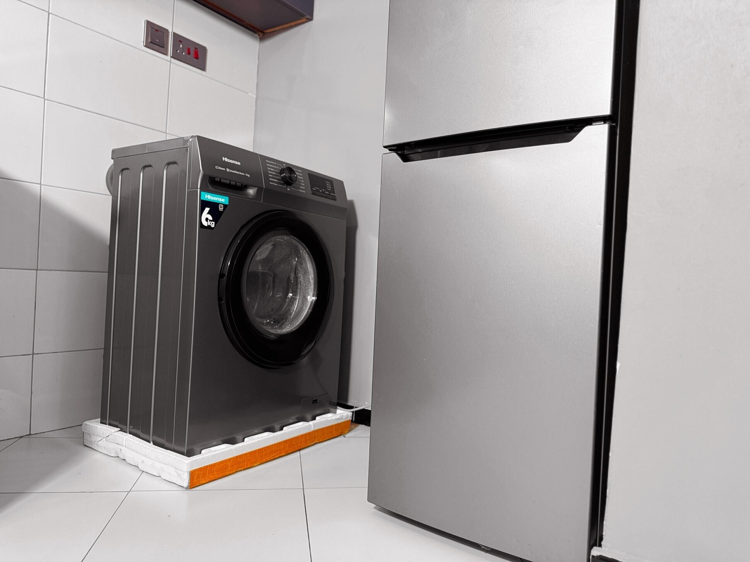 A compact, modern laundry room with a front-loading washing machine and a stainless steel refrigerator.