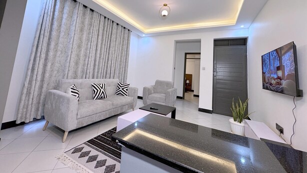 A modern living room with a sofa, coffee table, and a TV mounted on the wall. - RD Homes Bunga (Kampala)