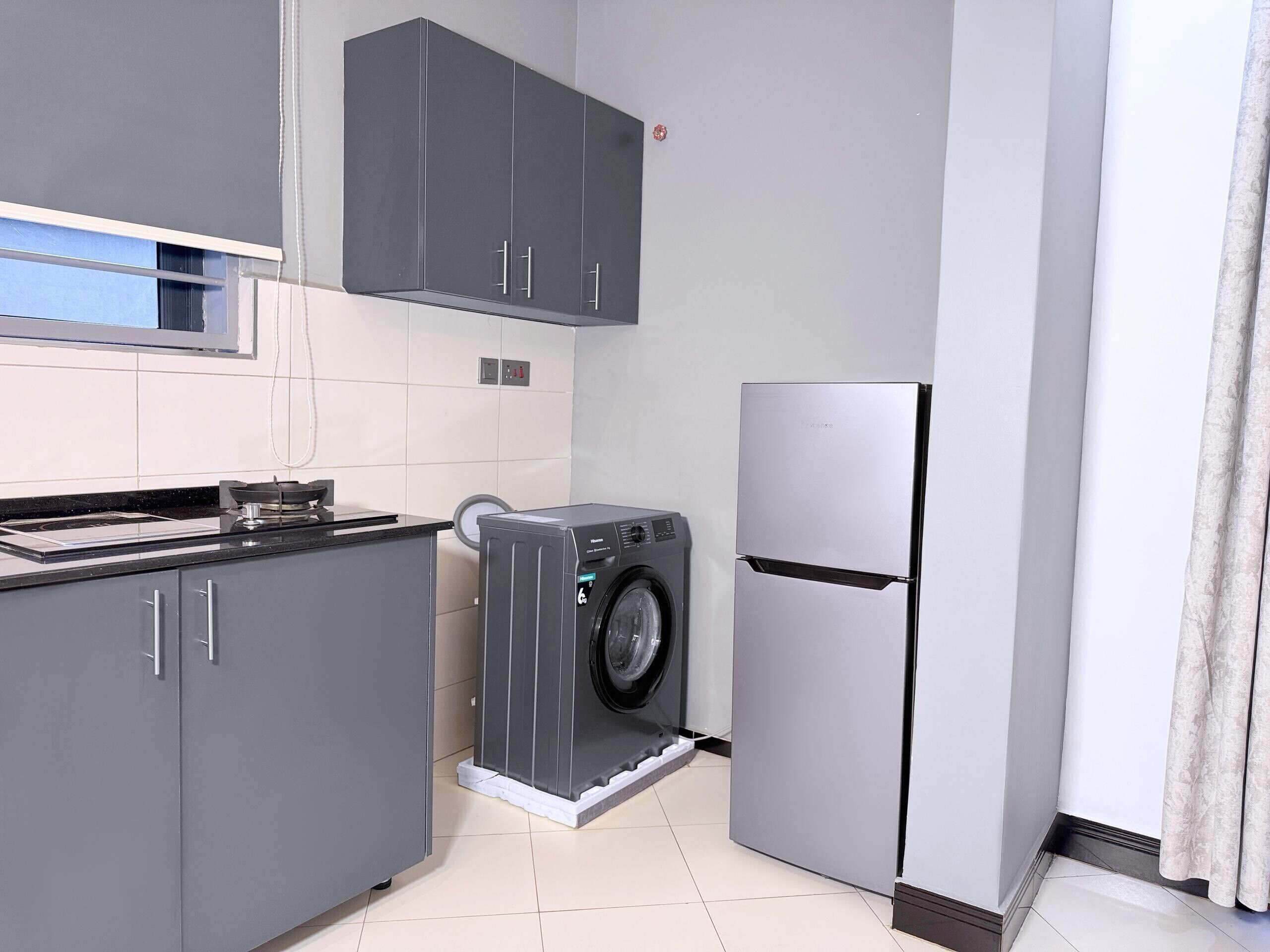 A compact kitchen with grey cabinets, a built-in washing machine, and a stainless steel refrigerator.