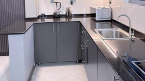 A modern kitchen with grey cabinets, a black countertop, a built-in sink, and a kettle. - RD Homes Bunga (Kampala)