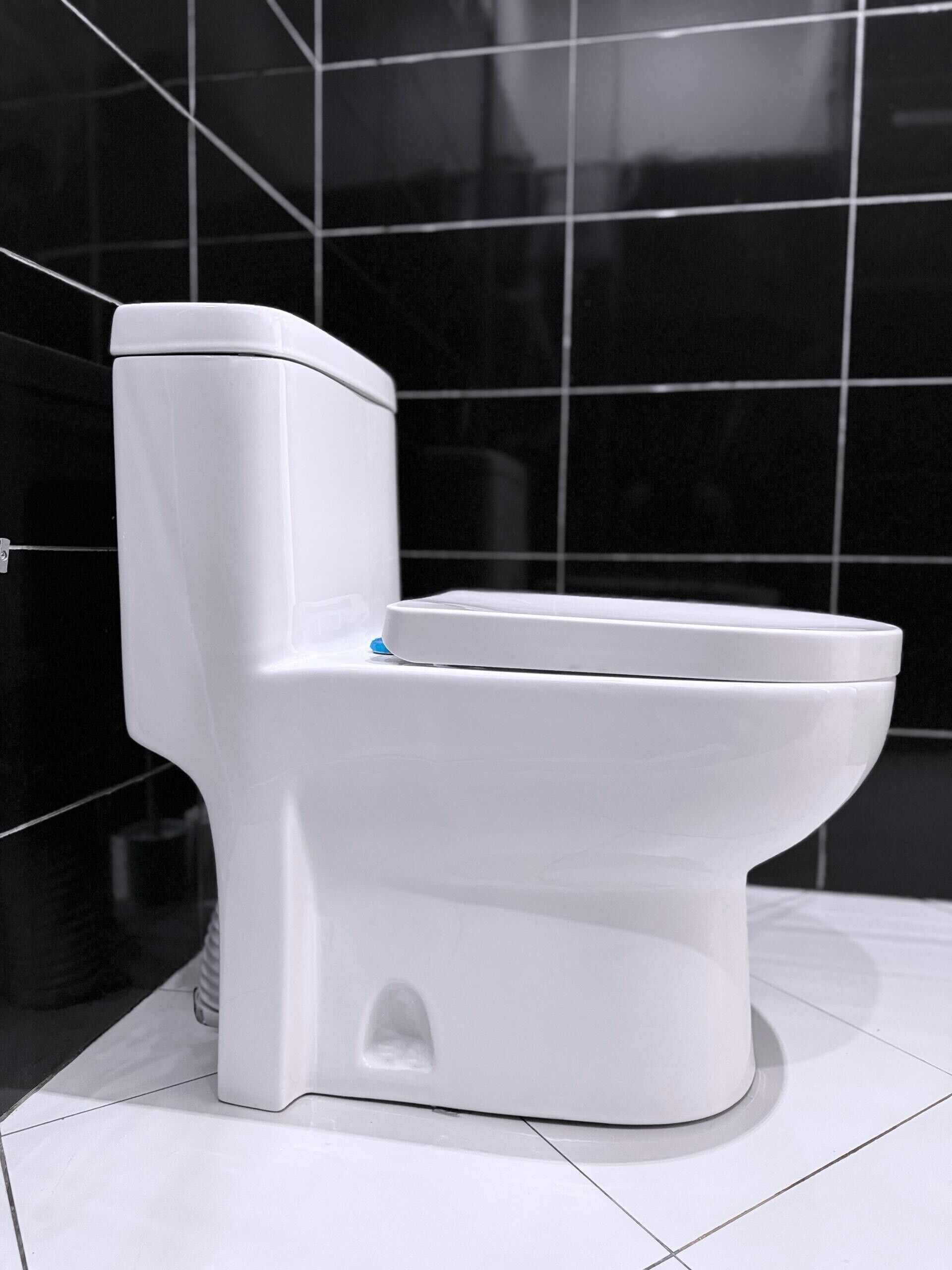 Eine weiße Toilette in einem Badezimmer mit schwarzen Fliesenwänden.