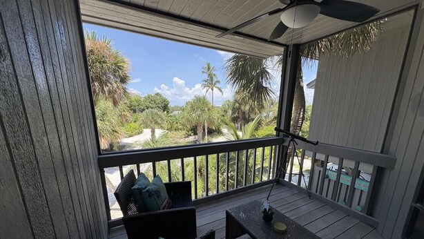 A covered outdoor seating area with a table and chairs, overlooking a tropical landscape with palm trees and a clear sky.
