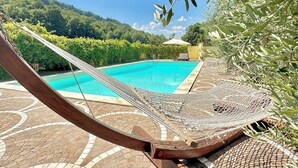 A hammock by a pool with a tiled patio and a view of a lush green landscape. - Villa of Silence-Peace and Wellness in the Vineyards of Orvieto (Umbria)