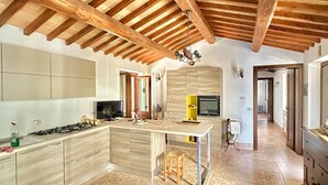 A spacious kitchen with a central island, wooden beams on the ceiling, and patterned floor tiles. - Villa of Silence-Peace and Wellness in the Vineyards of Orvieto (Umbria)