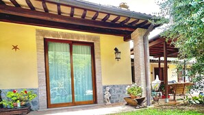 A building with a yellow facade, large sliding glass doors, and a covered patio area with potted plants and outdoor furniture. - Villa of Silence-Peace and Wellness in the Vineyards of Orvieto (Umbria)