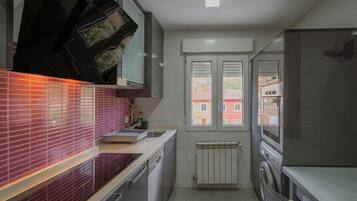 Een kleine keuken met een inbouwoven, een wasmachine en een raam met uitzicht op gebouwen.