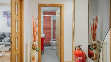 Een gang die uitkomt bij een badkamer met rode tegels, een wit toilet en een brandblusser.