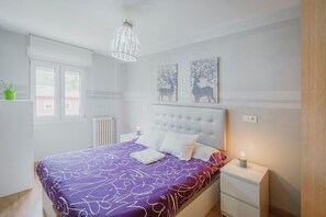 Un dormitorio con cama, mesitas de noche, radiador, ventana y obras de arte en la pared.