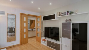 Een moderne woonkamer met een flatscreen televisie, houten vloeren, een boekenkast en een schuifdeurkast.