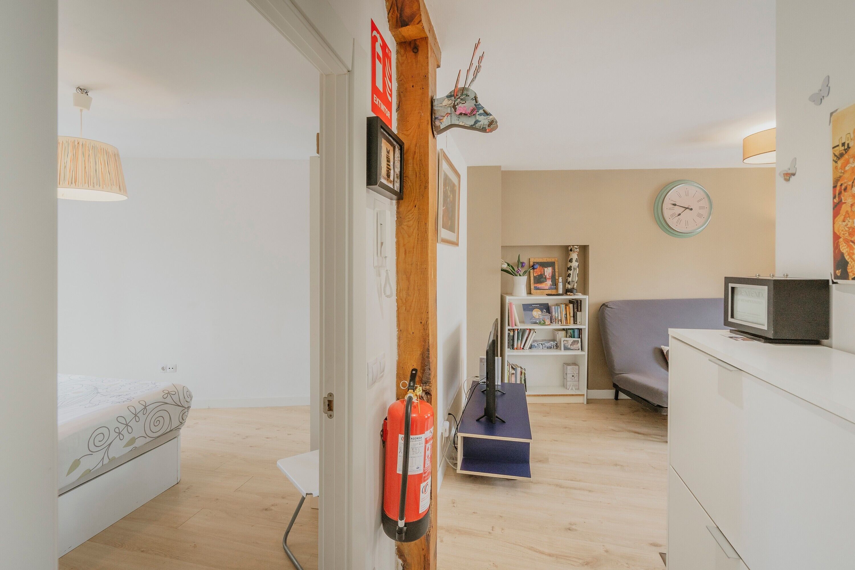 Una habitación con cama, escritorio, estantería, televisor y extintor.