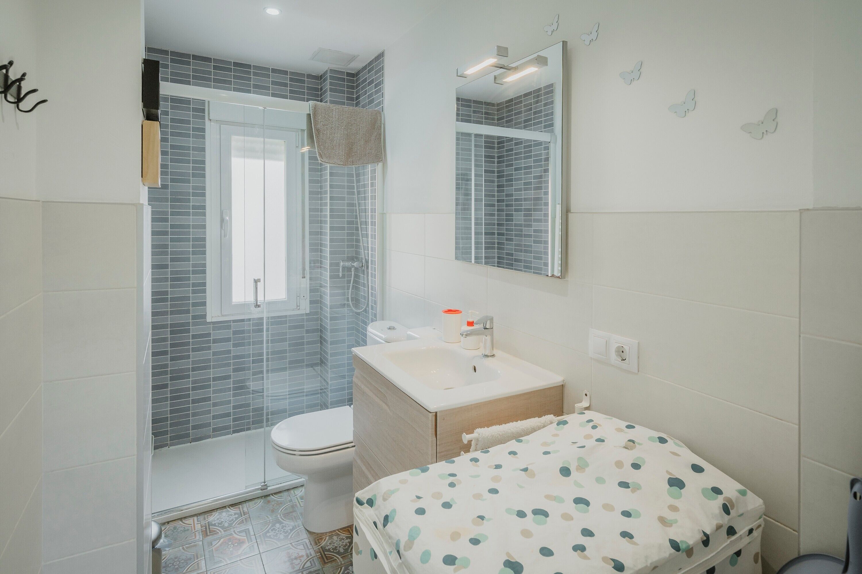 Une salle de bain avec douche, toilettes, lavabo, et un lit recouvert d’une couvre-lit à pois.