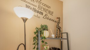 A wall with a 'Welcome' sign in multiple languages, a floor lamp, a shelf with a plant, and a giraffe decoration. - Apartment 'Loló Vut' with Wi-Fi (Burgos)