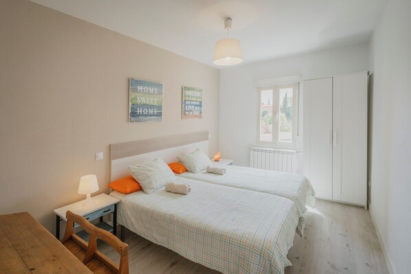 Une chambre avec deux lits, une table en bois, une table de chevet avec une lampe et une fenêtre donnant sur un beau paysage.