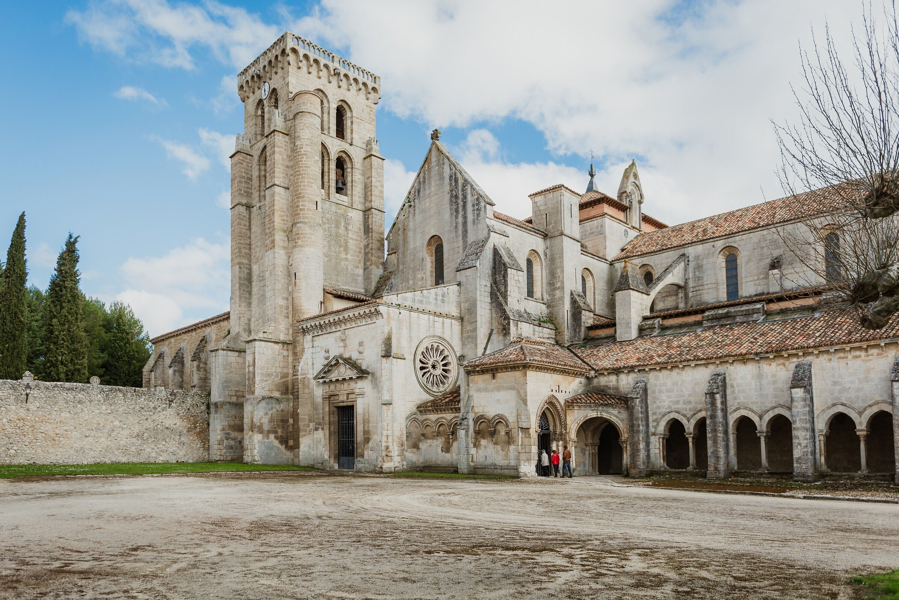 Una iglesia histórica con un campanario alto, un ventanal circular grande y un patio con suelo empedrado.