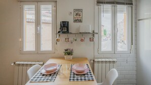 A dining area with a table set for two, a coffee machine, and a wall-mounted shelf with decorative items. - Apartment 'Loló Vut' with Wi-Fi (Burgos)