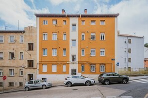 Un immeuble à plusieurs étages, doté d’une façade jaune, de nombreuses fenêtres et de voitures garées dans la rue.